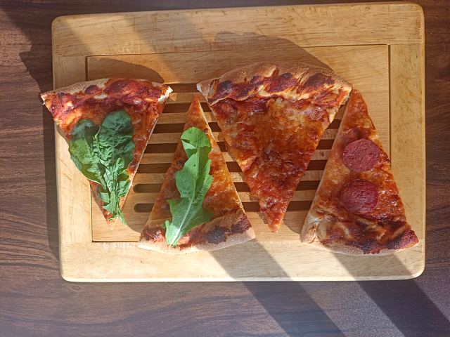 Cuatro porciones pequeñas de pizza con hojas de rúcula sobre una tabla de madera
