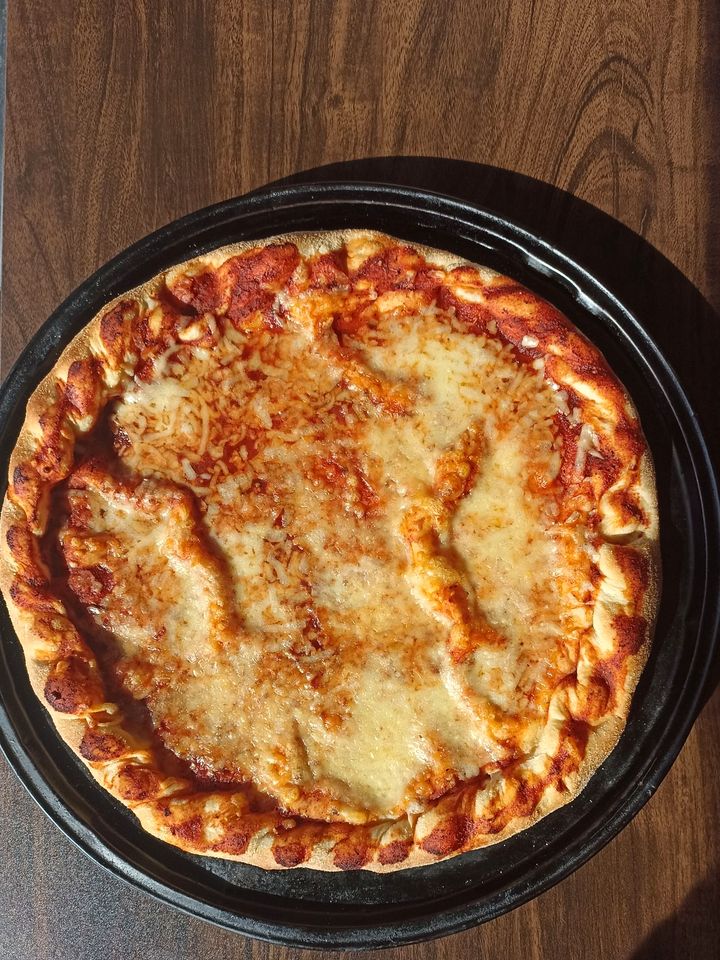 La misma bandeja sobre la misma mesa con la pizza ya horneada, el queso gratinado y el borde dorado