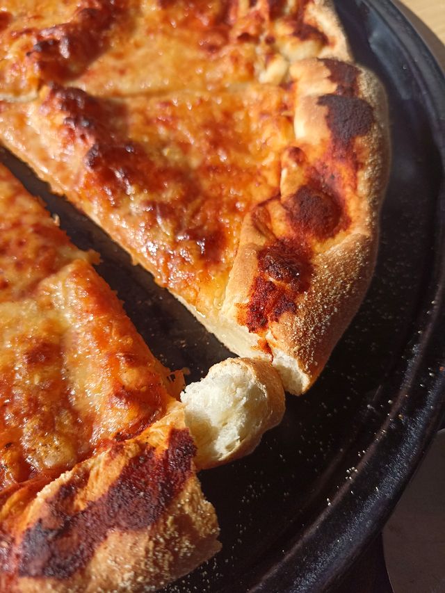 Una pizza cortada en la bandeja, con un trozo de borde separado y el queso gratinado
