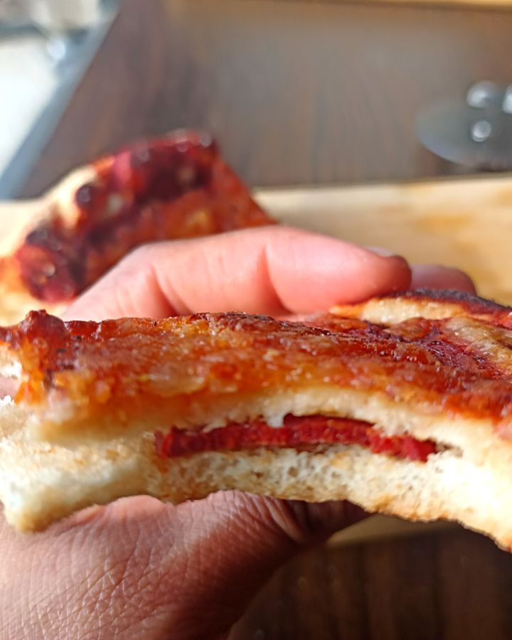 Una mano sostiene una porción de Pizzalvi con pepperoni, vista de corte