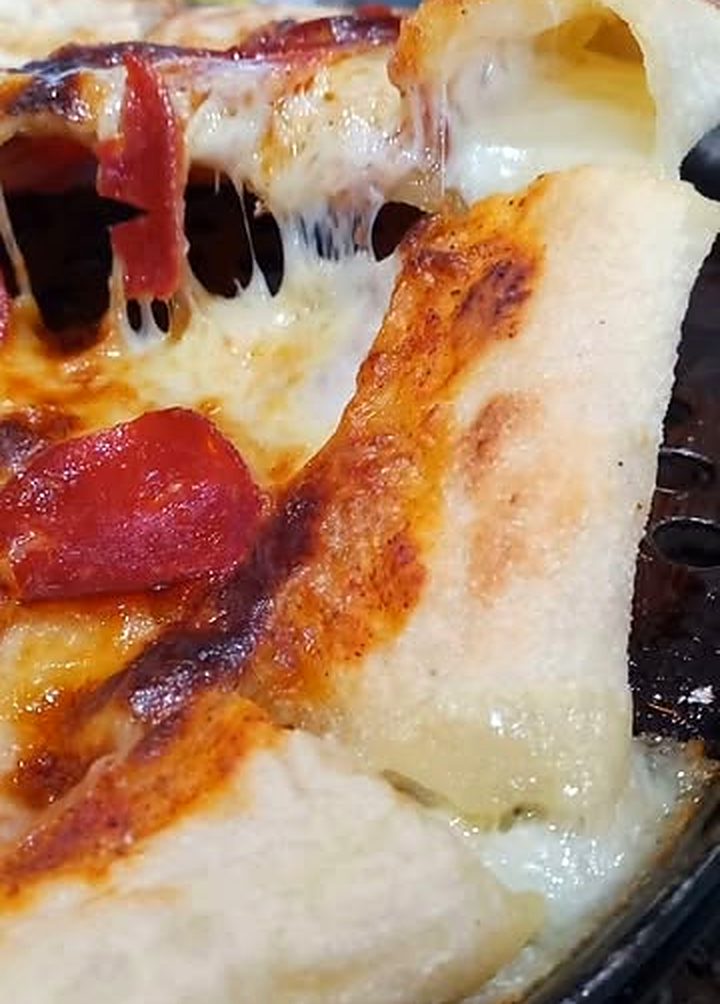 Una porción de Pizzalvi abierta por el borde, con queso fundido que se estira por dentro de la masa